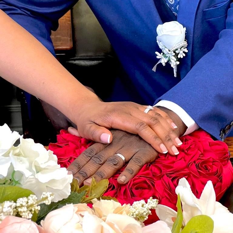 Close-up of bride and groom’s hands with wedding rings resting on vibrant red roses, captured by a London wedding photographer.